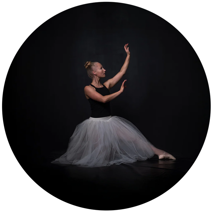 Ballerina in a black top and white tutu against a dark background